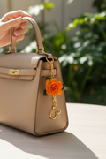 Orange rose charm attached to handbag - lifestyle photo showing use as bag accessory